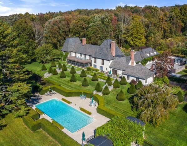 Aerial view of a large house with a pool and manicured lawn surrounded by trees.