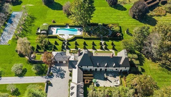 Aerial view of a large estate with a white house, pool, and manicured lawns.