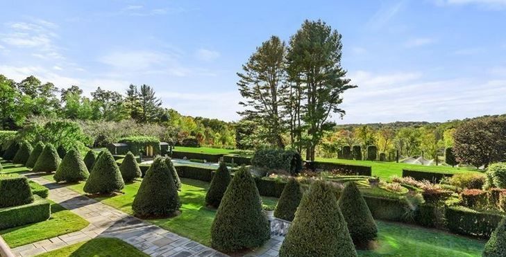 Formal garden with cone-shaped shrubs, manicured lawns, trees, and a blue sky.
