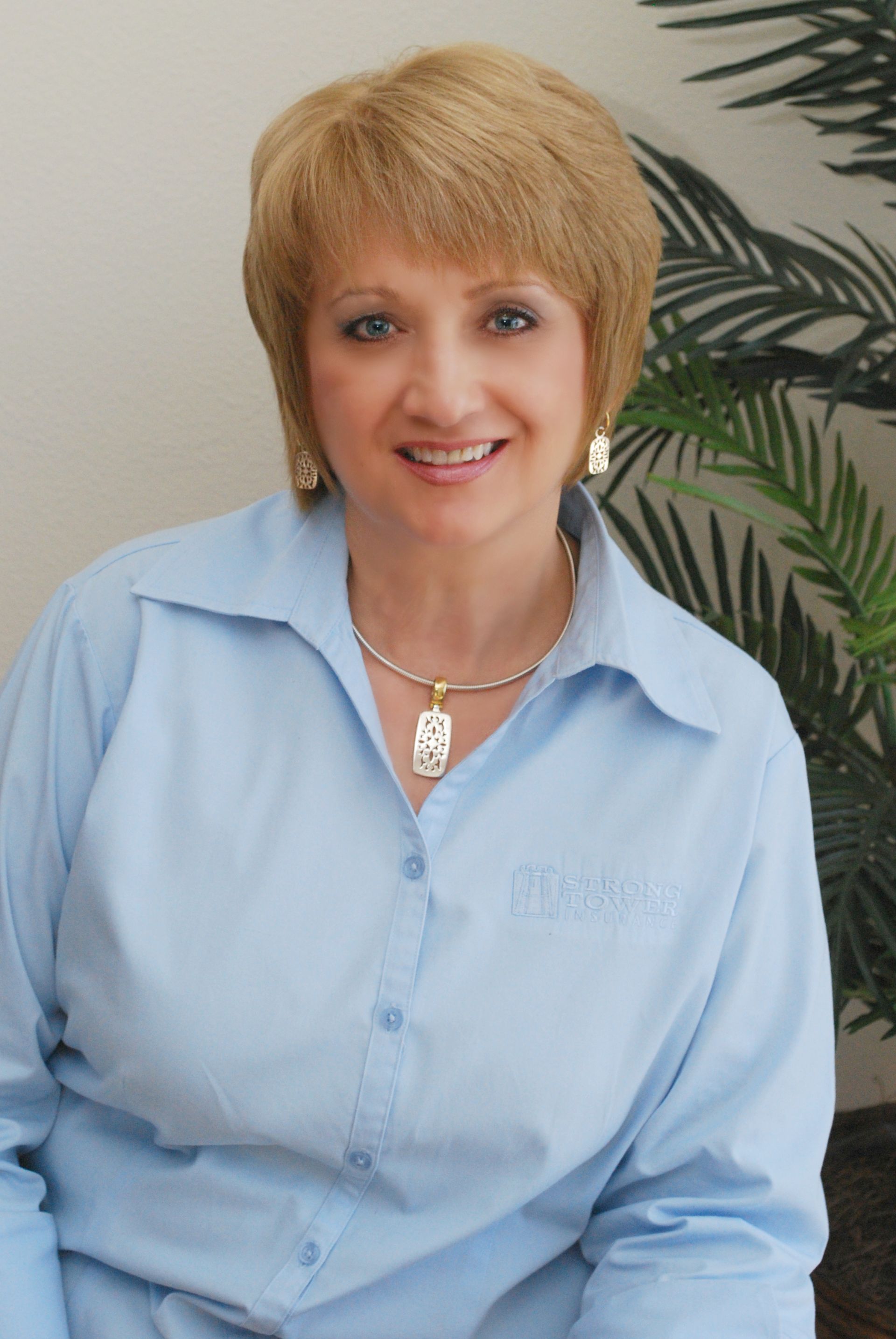 Woman with brown hair smiles in front of a backdrop with the Alphindrop Insurance logo. She wears a white shirt.