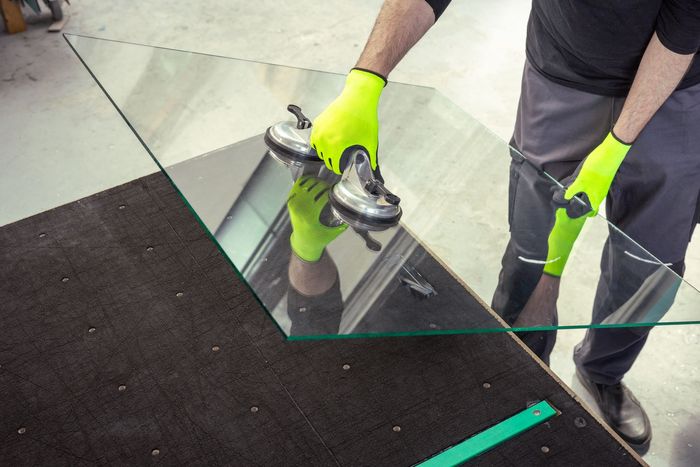 A man wearing neon yellow gloves is holding a piece of glass.