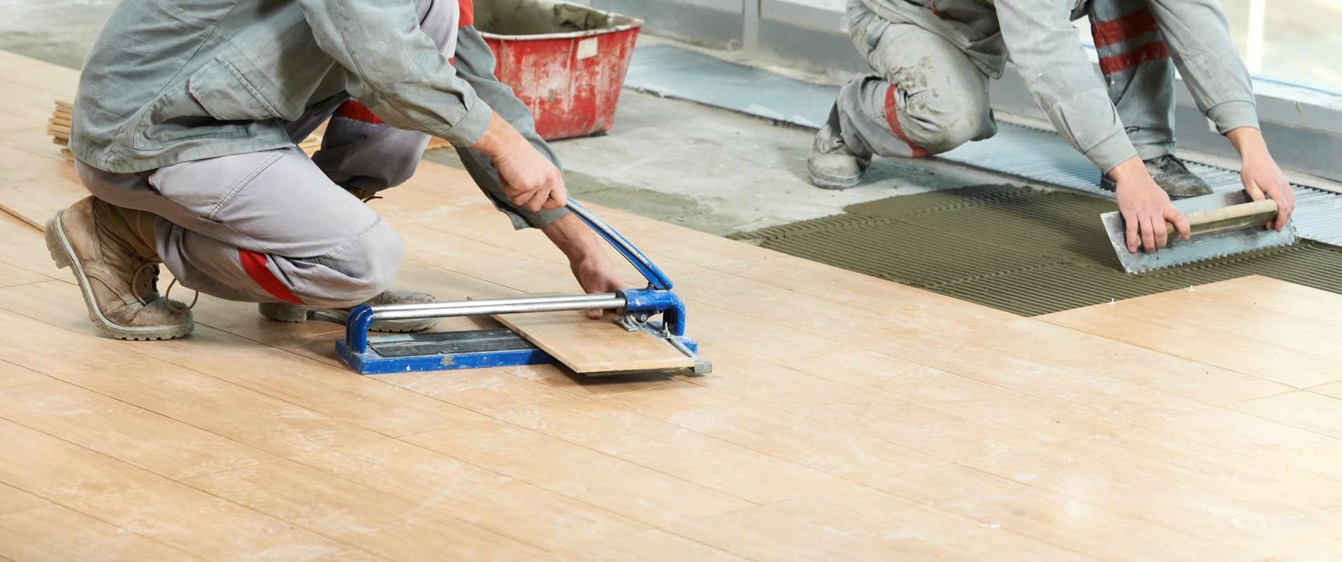 Two men are installing tiles on a wooden floor.