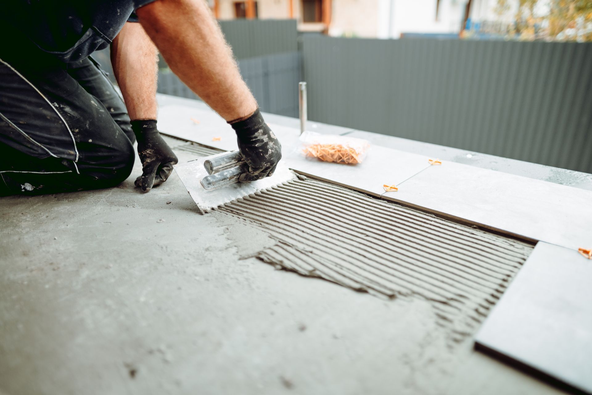 A man is laying tiles on a concrete floor.