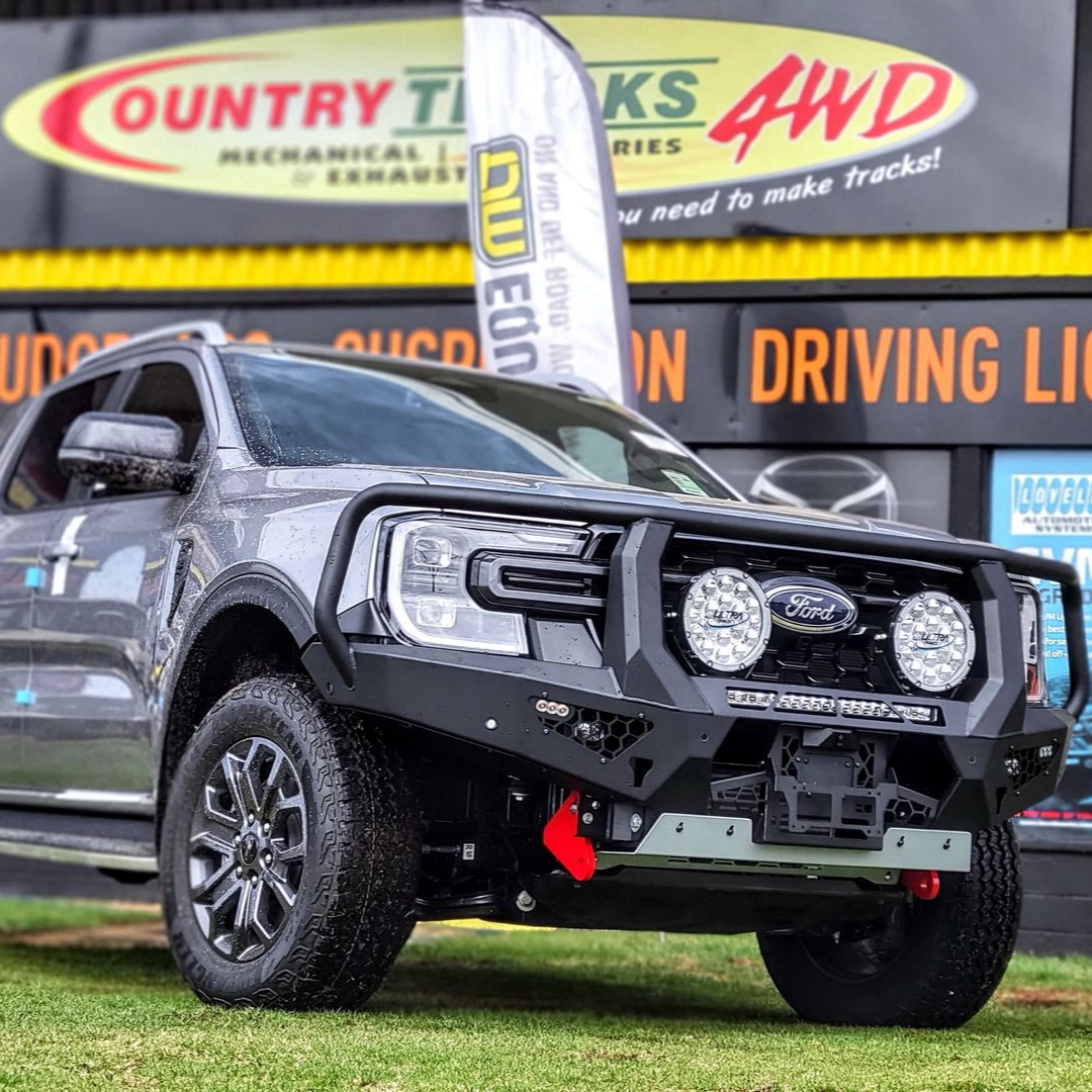 Blue off-road truck with a silver bull bar, spotlights, and black wheels in a sunny outdoor setting.