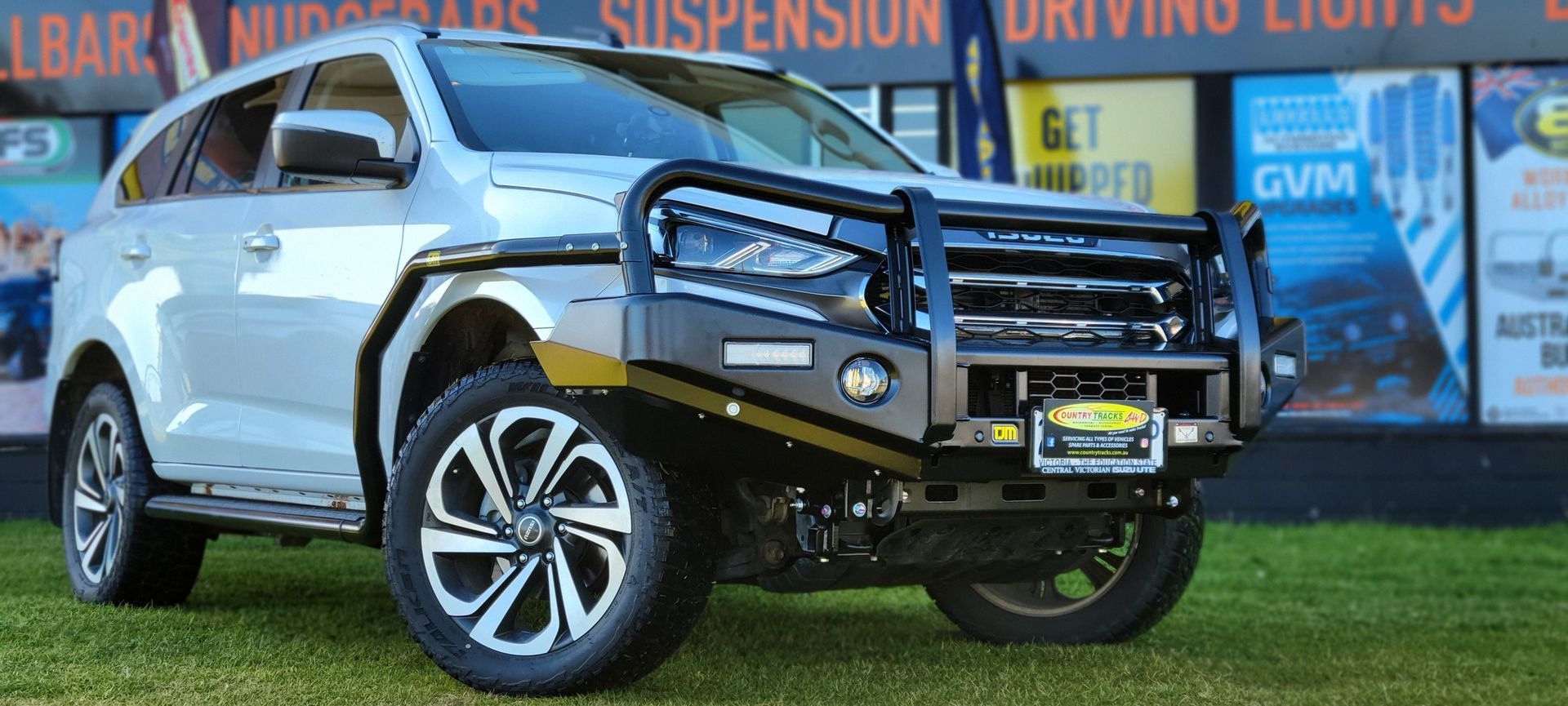 Silver 4x4 truck with a black bull bar, snorkel, and side steps parked outside a store.