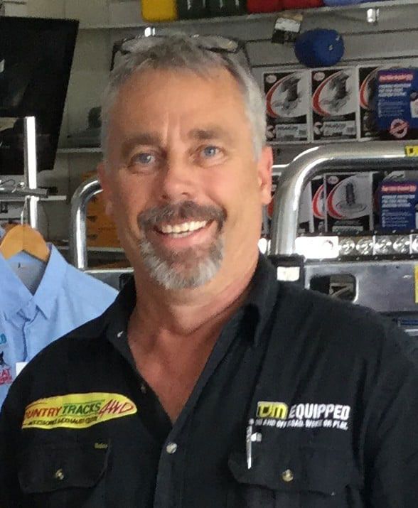 Man with grey hair and goatee, smiling at the camera, in a store. He's wearing a black shirt with logos.