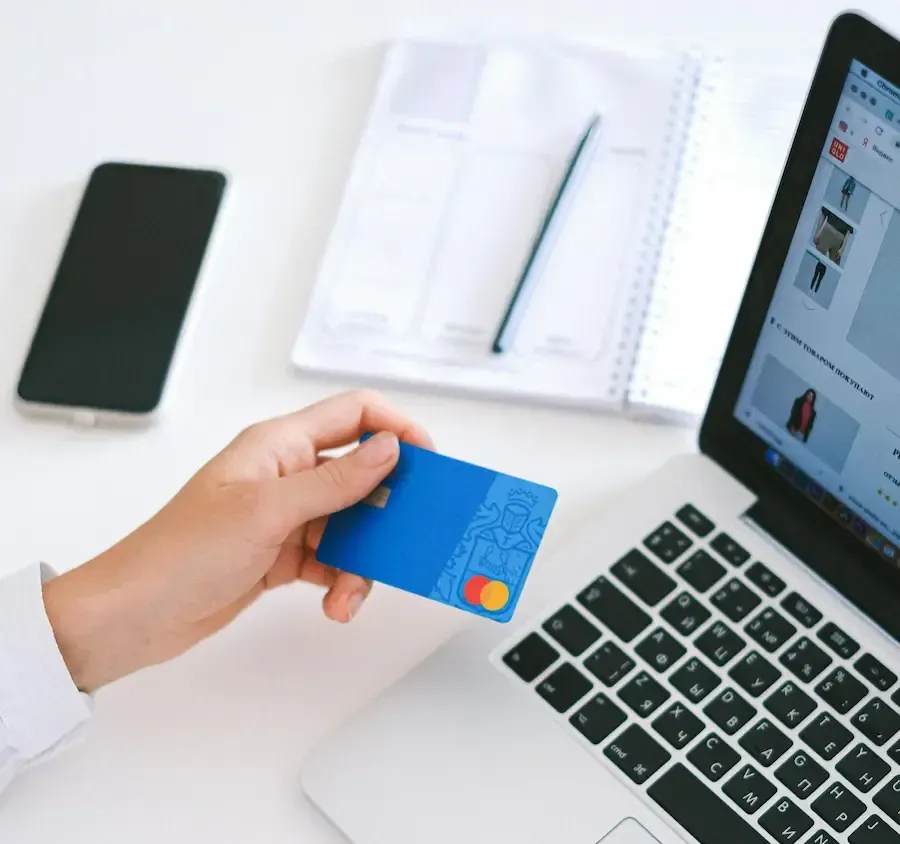 Hand holding a credit card in front of an e-commerce site on a computer.