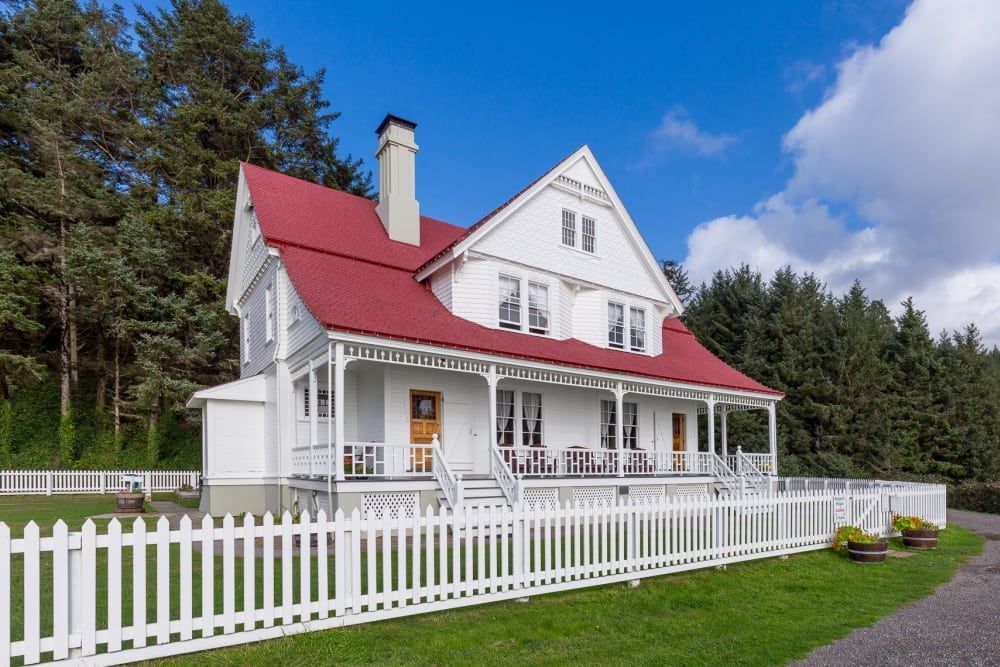 A large white house with a red roof and a white picket fence surrounding it.