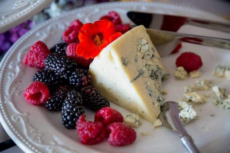 A white plate topped with raspberries , blackberries and a slice of cheese.