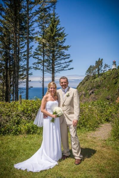 A bride and groom are posing for a picture in front of a lighthouse.