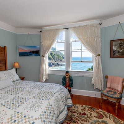 A bedroom with a bed , chair , rug and a window overlooking the ocean.