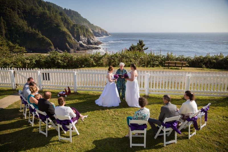A bride and groom are getting married in front of a white picket fence overlooking the ocean.
