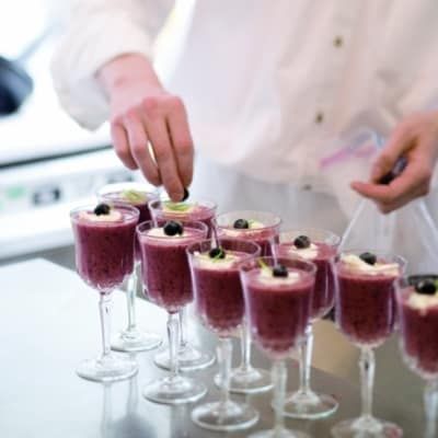 A person is preparing purple desserts in wine glasses