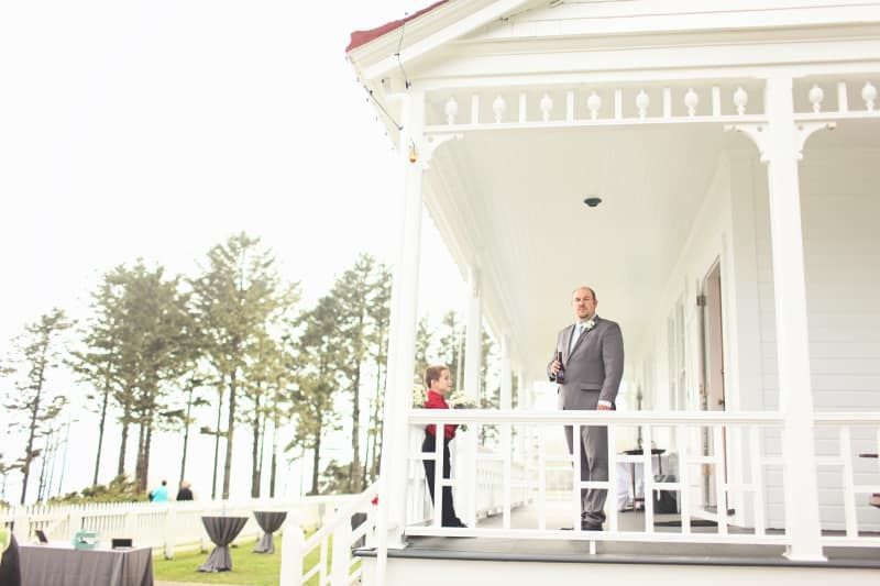A man in a suit is standing on the porch of a white house.