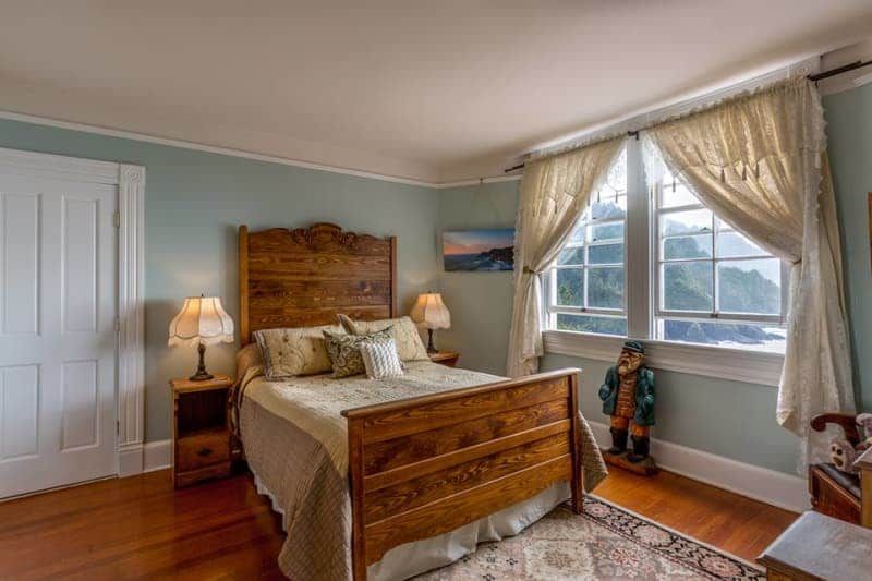 A bedroom with a wooden bed , two nightstands , two lamps and two windows.