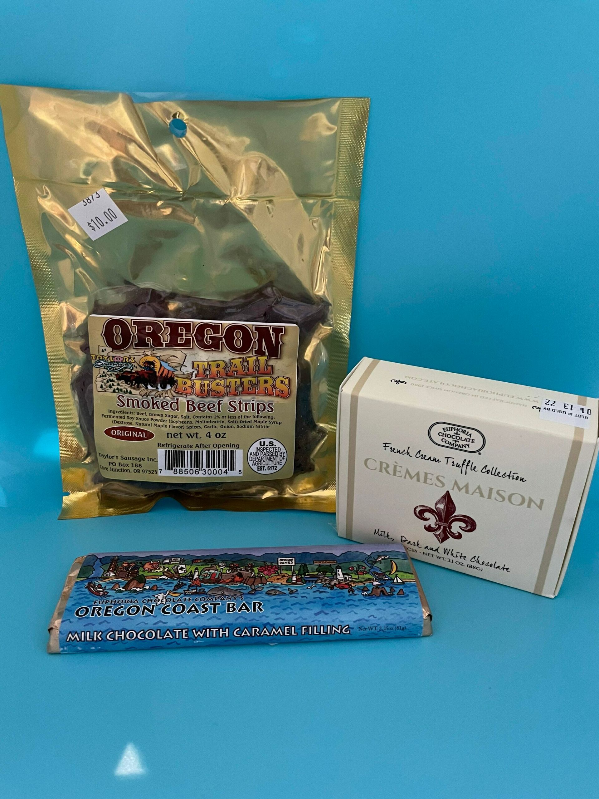 A bag of beef jerky , a bar of chocolate , and a box of cigarettes are on a blue table.