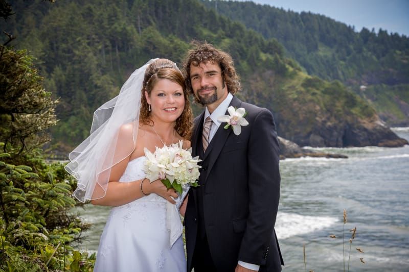A bride and groom are posing for a picture in front of the ocean.