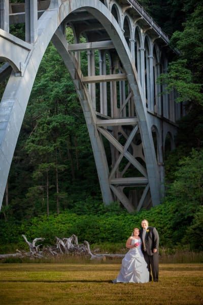A bride and groom are posing for a picture in front of a bridge.