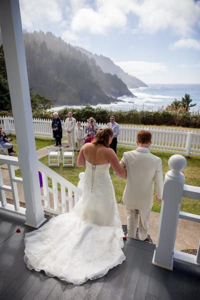 A bride and groom are standing on a porch holding hands.