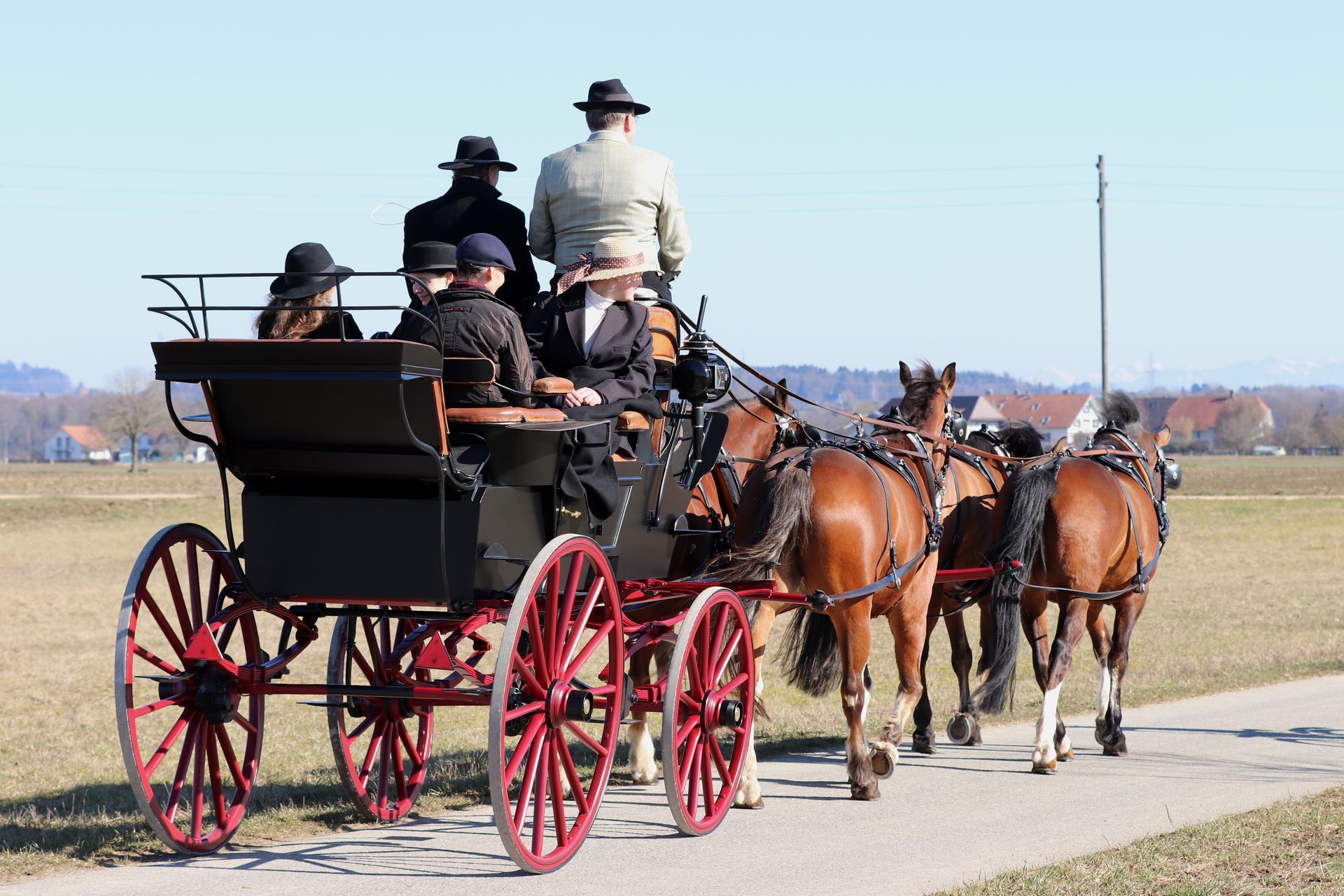 Eine von vier braunen Pferden gezogene Pferdekutsche mit mehreren Personen fährt auf einer Straße.