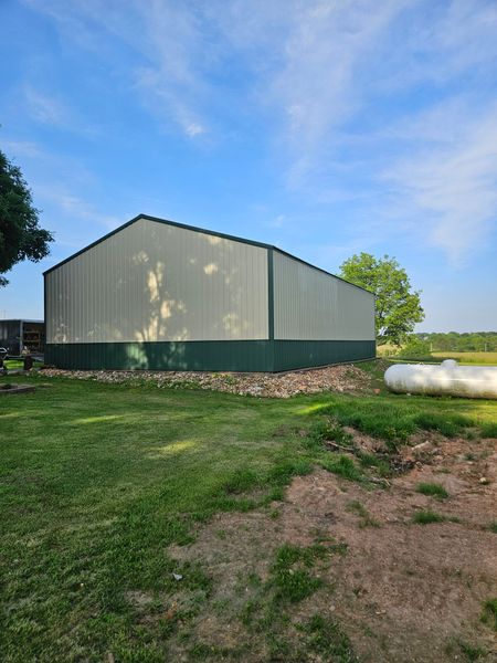Large metal building with green trim, on a grassy area, with blue sky.