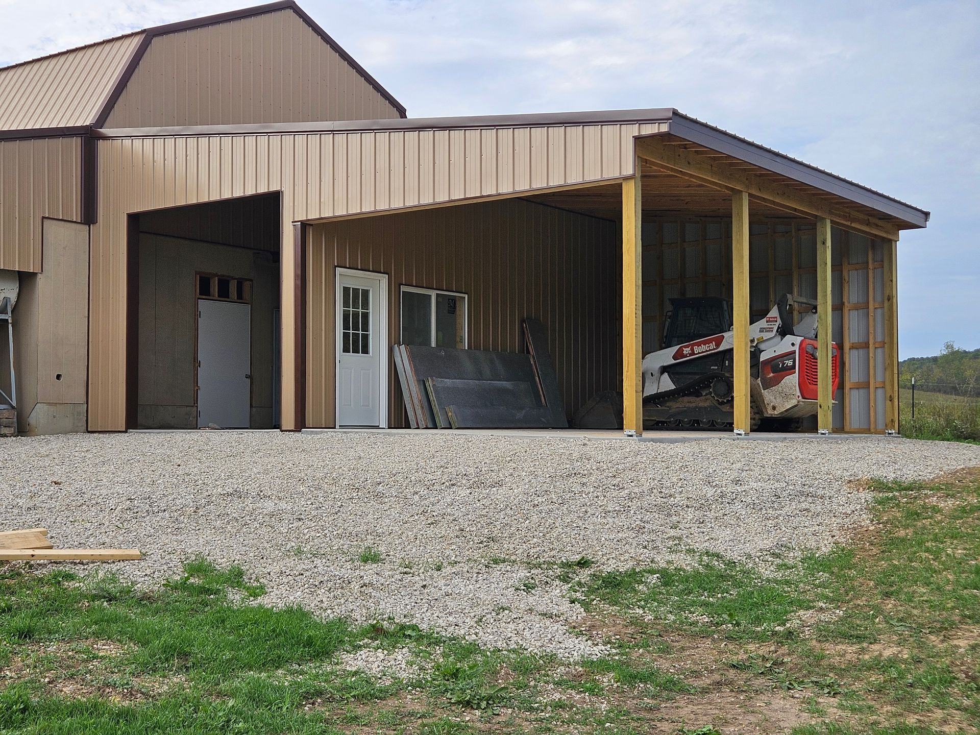 Tan metal building with open carport, gravel base, and UTV.