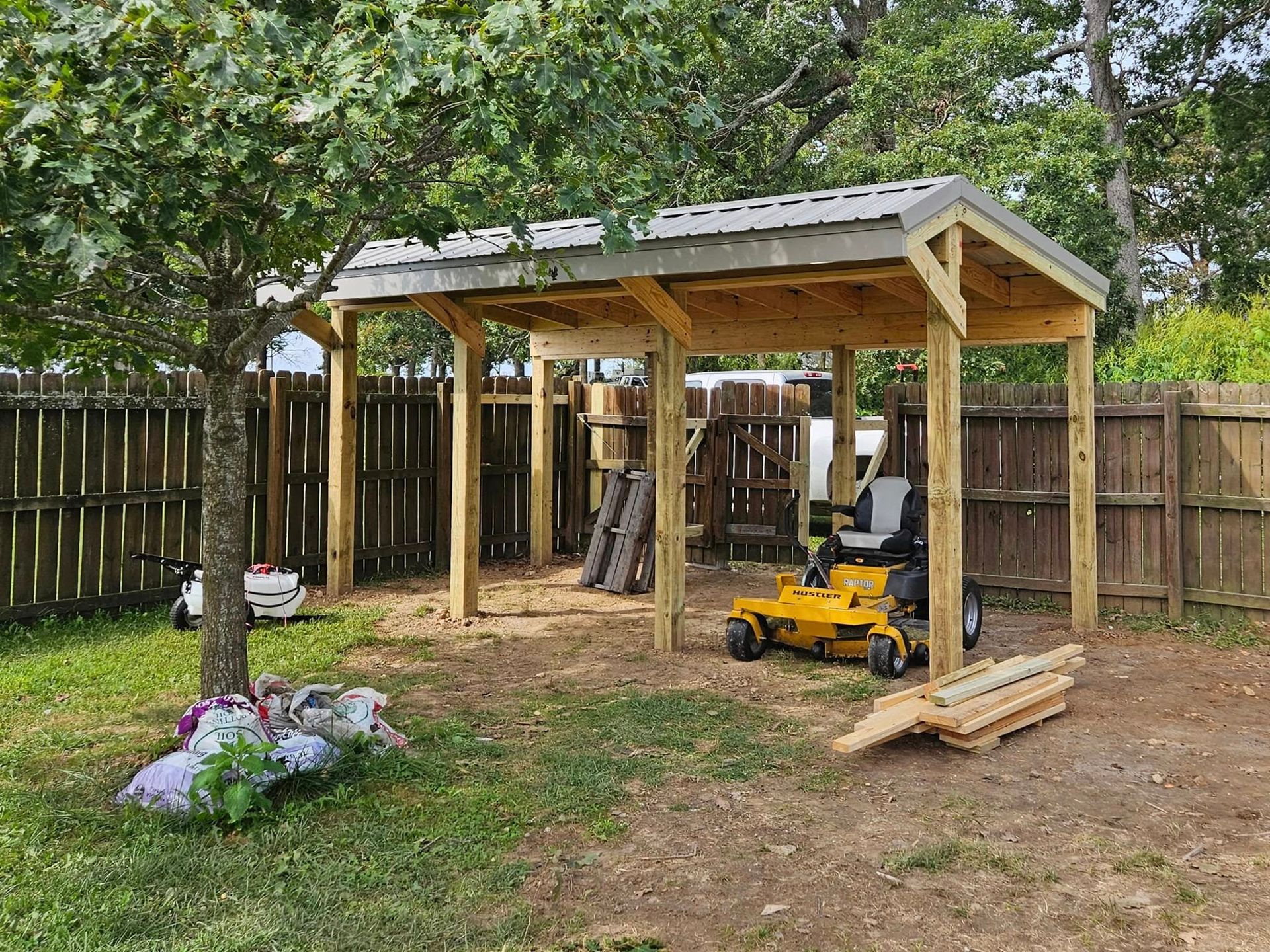 Wooden shed with a riding lawnmower parked inside. Trees and a fence surround the grassy yard.
