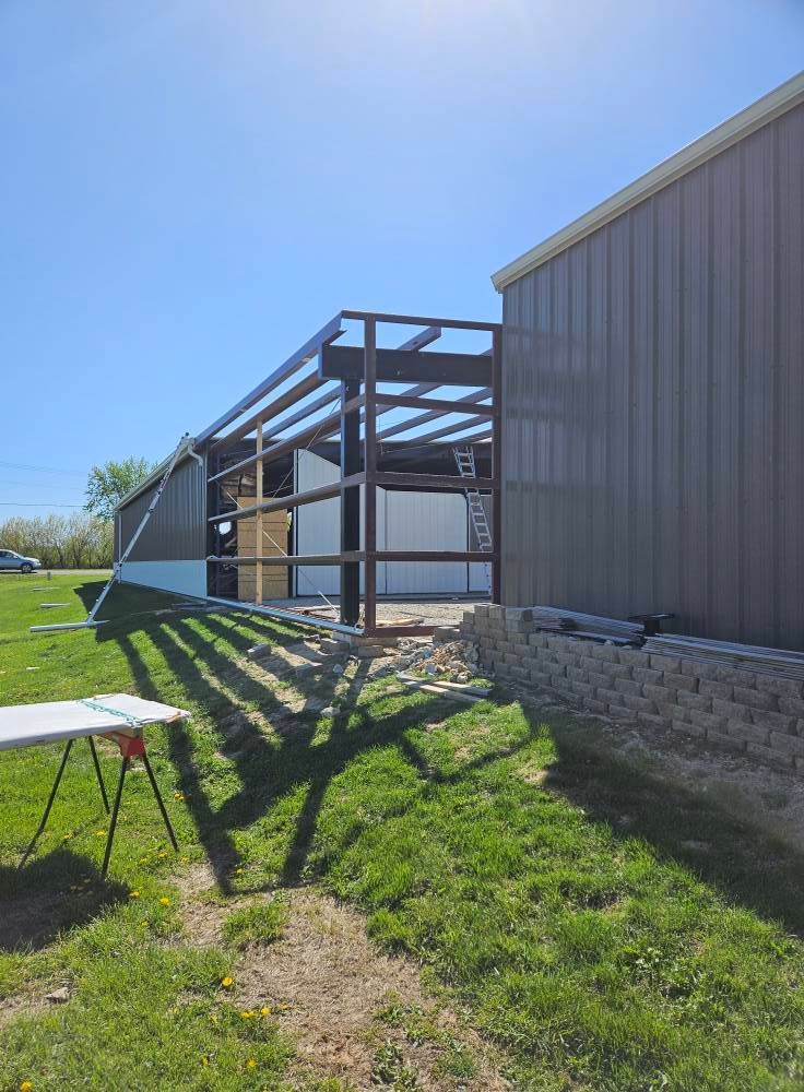 Steel frame construction attached to a brown and white building. Sunny, green grass in foreground.