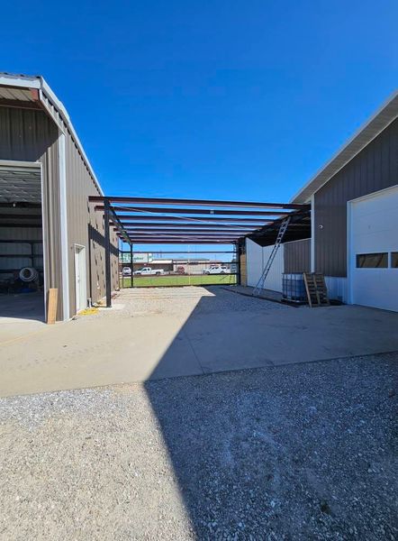 Steel framework for a covered area being built between two gray buildings on a sunny day.