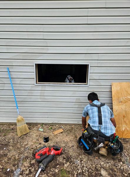 Two construction workers installing a window in a gray-sided building.