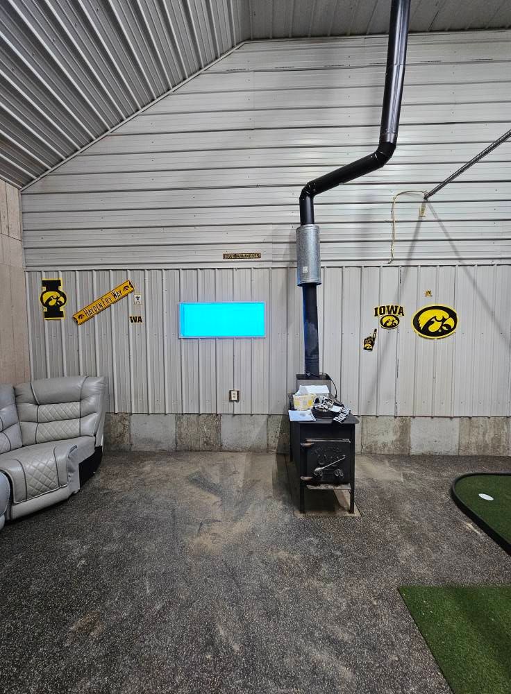 Interior with wood-burning stove and black chimney against a white corrugated metal wall. Includes a couch and golf mat.