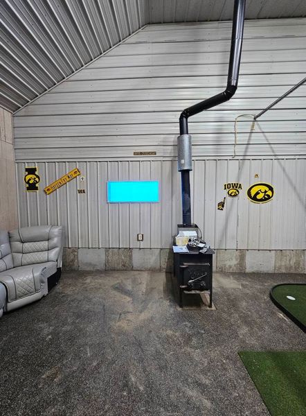 Interior with wood-burning stove and black chimney against a white corrugated metal wall.