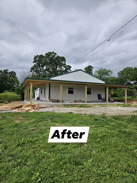 Newly built house with green metal roof, a porch, and siding, set in a grassy field under a cloudy sky.