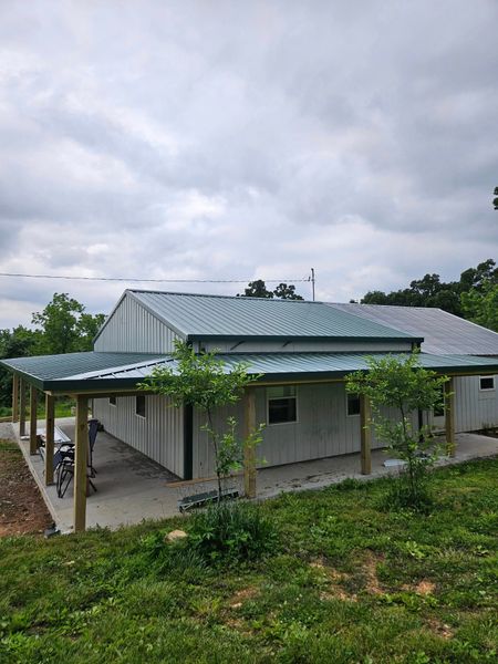 Gray metal-roofed building with covered porch. Green trees and cloudy sky in the background.