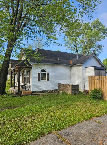 White house with porch, brown shutters, and attached garage under a blue sky, surrounded by green grass and trees.