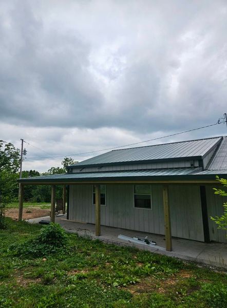 A light-colored building with a covered porch and gray metal roof under a cloudy sky.