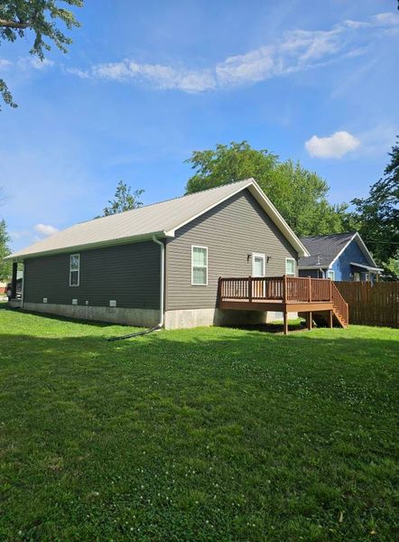 Side view of a gray house with a wooden deck, against a blue sky with green grass in the foreground.