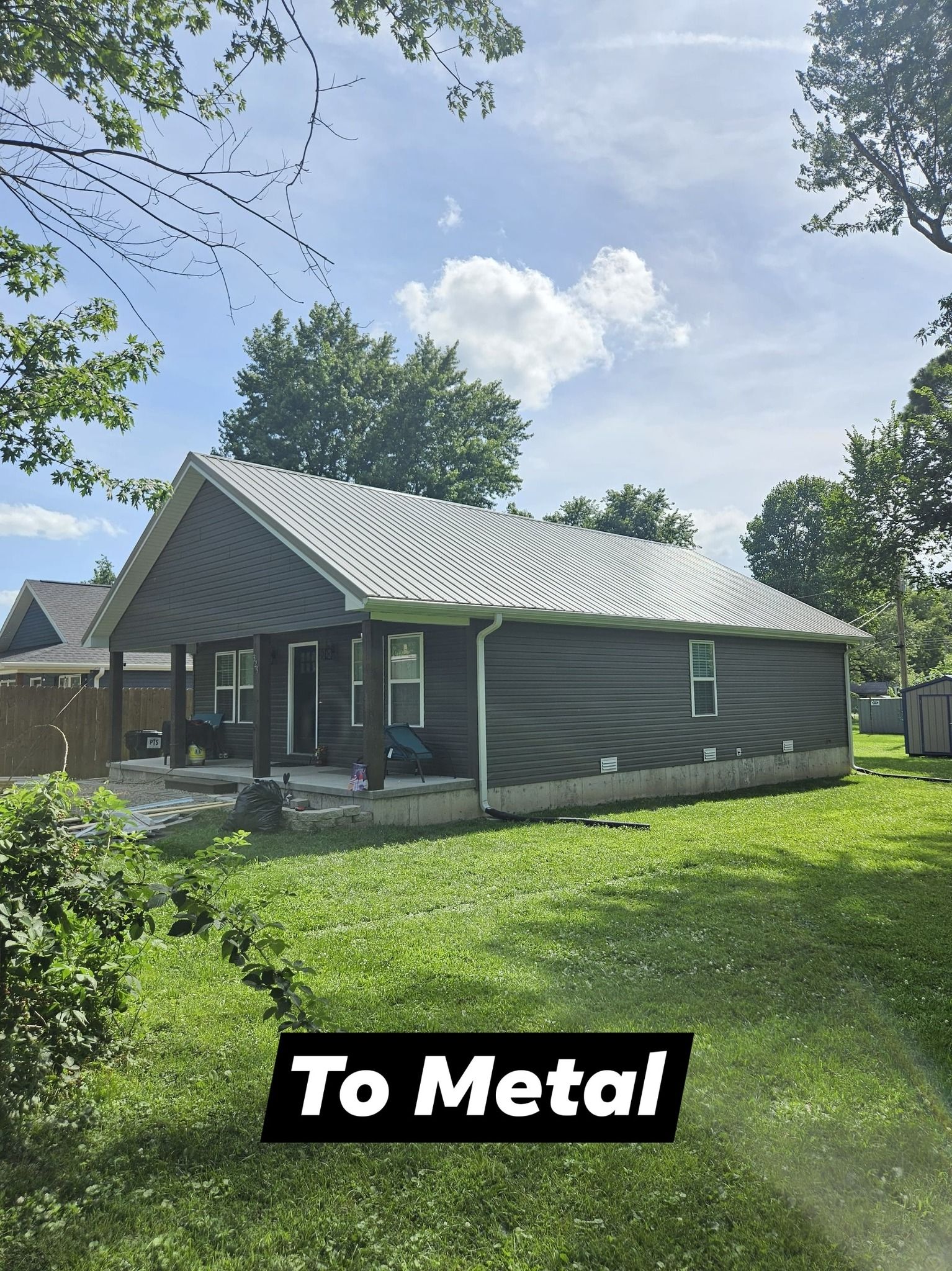 A house with a gray metal roof and siding, set in a grassy yard, under a blue sky.