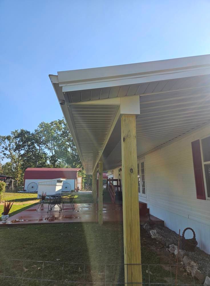 A covered porch on a white house with wooden support beams. Red shed and yard in the background.