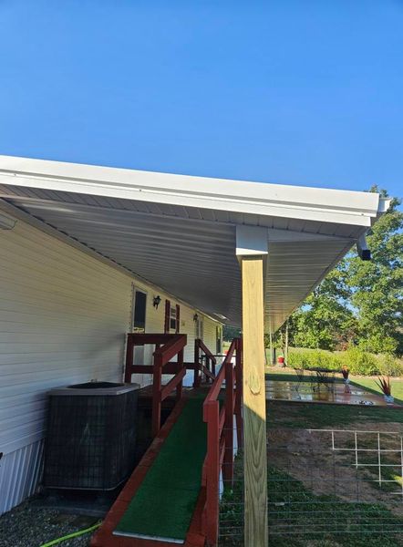 A building with a covered ramp and a/c unit; green ramp surface, blue sky, and a grassy area.