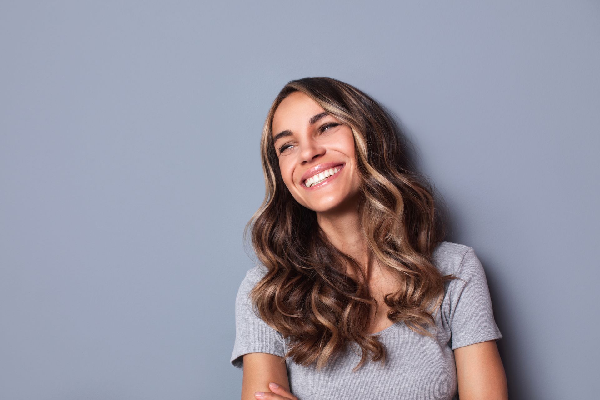 A woman with long hair is smiling against a gray background.