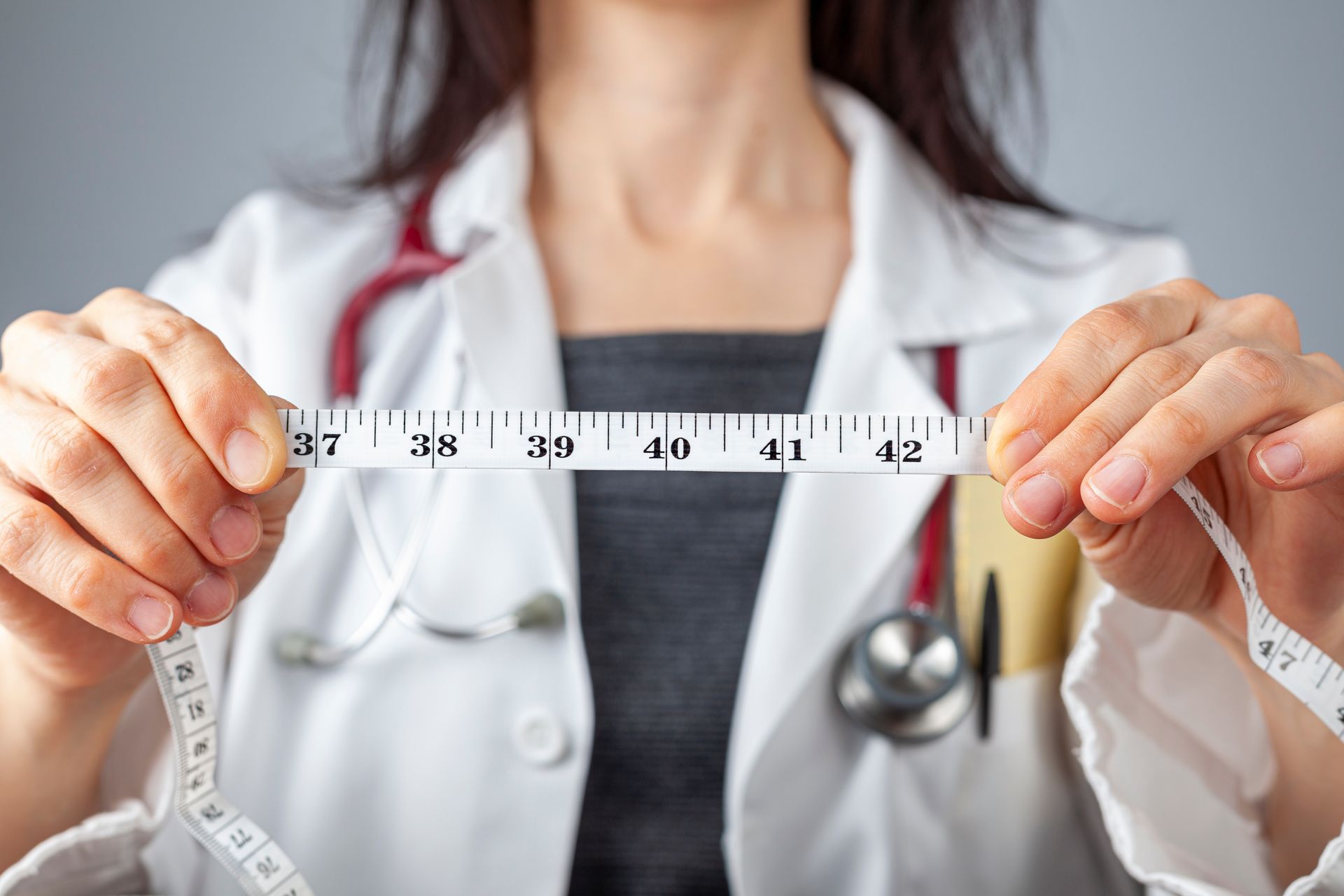 Doctor holding a measuring tape around their neck, measuring waist circumference in a clinic.