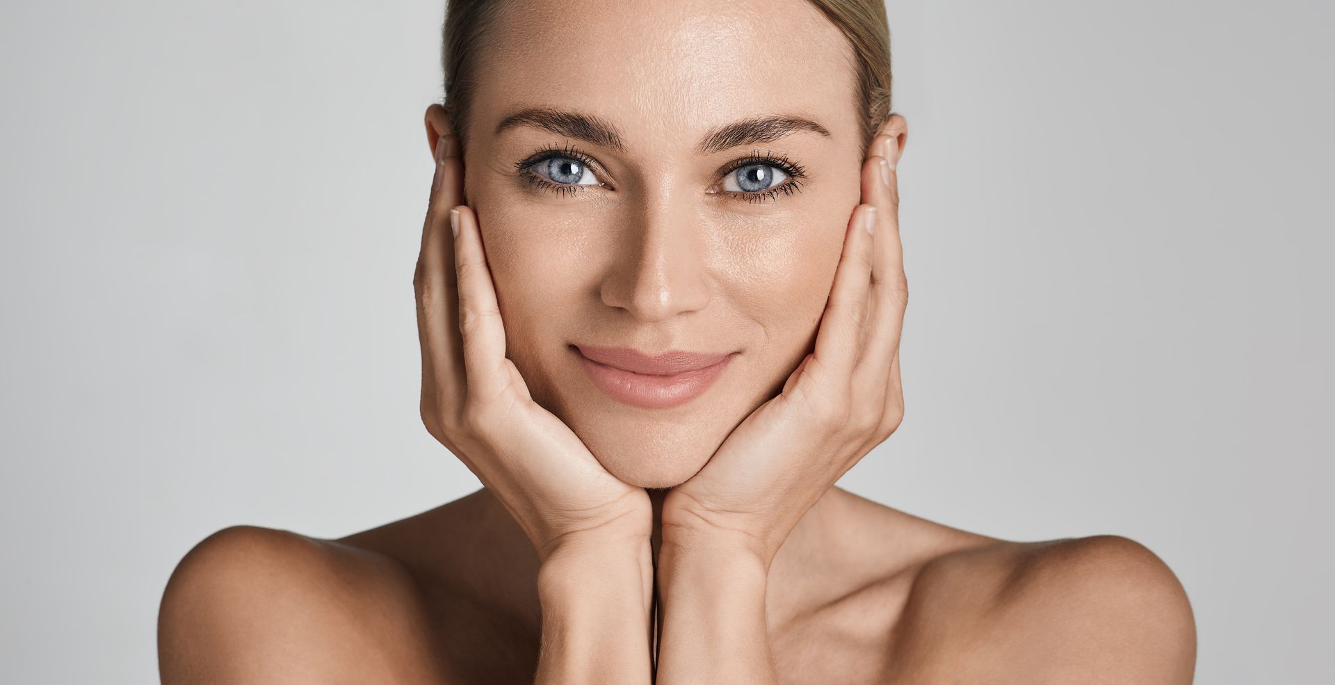 Portrait of a smiling person with hands on cheeks against a light gray background