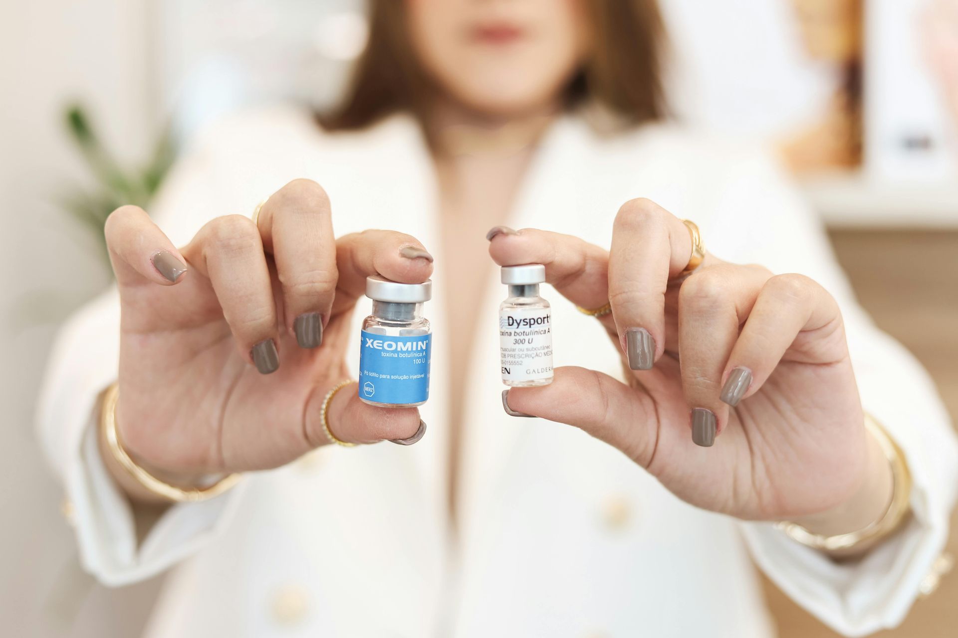 Hands holding two small vaccine vials, one blue label and one clear label, against a blurred white background