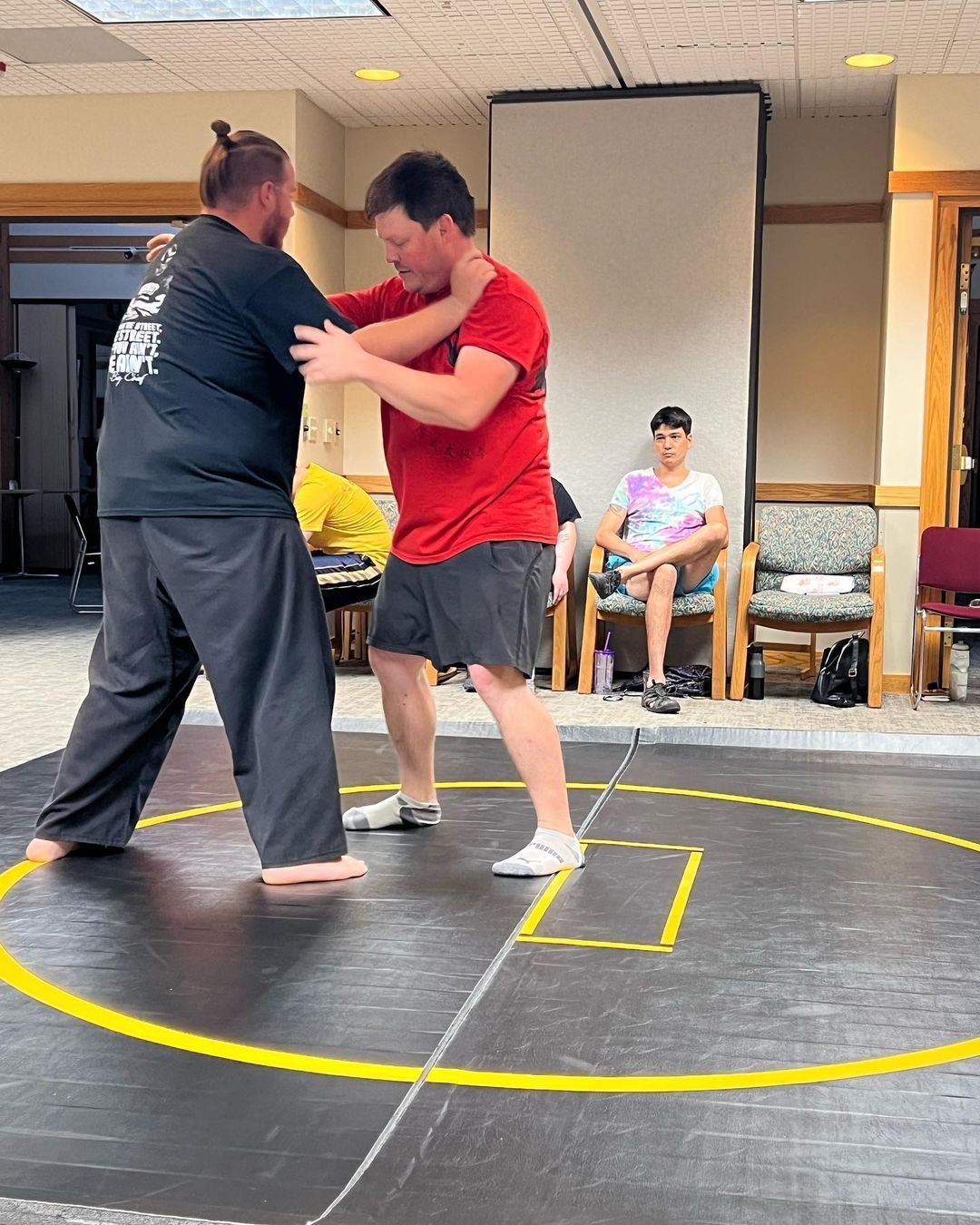 Two men are wrestling on a wrestling mat in a room.
