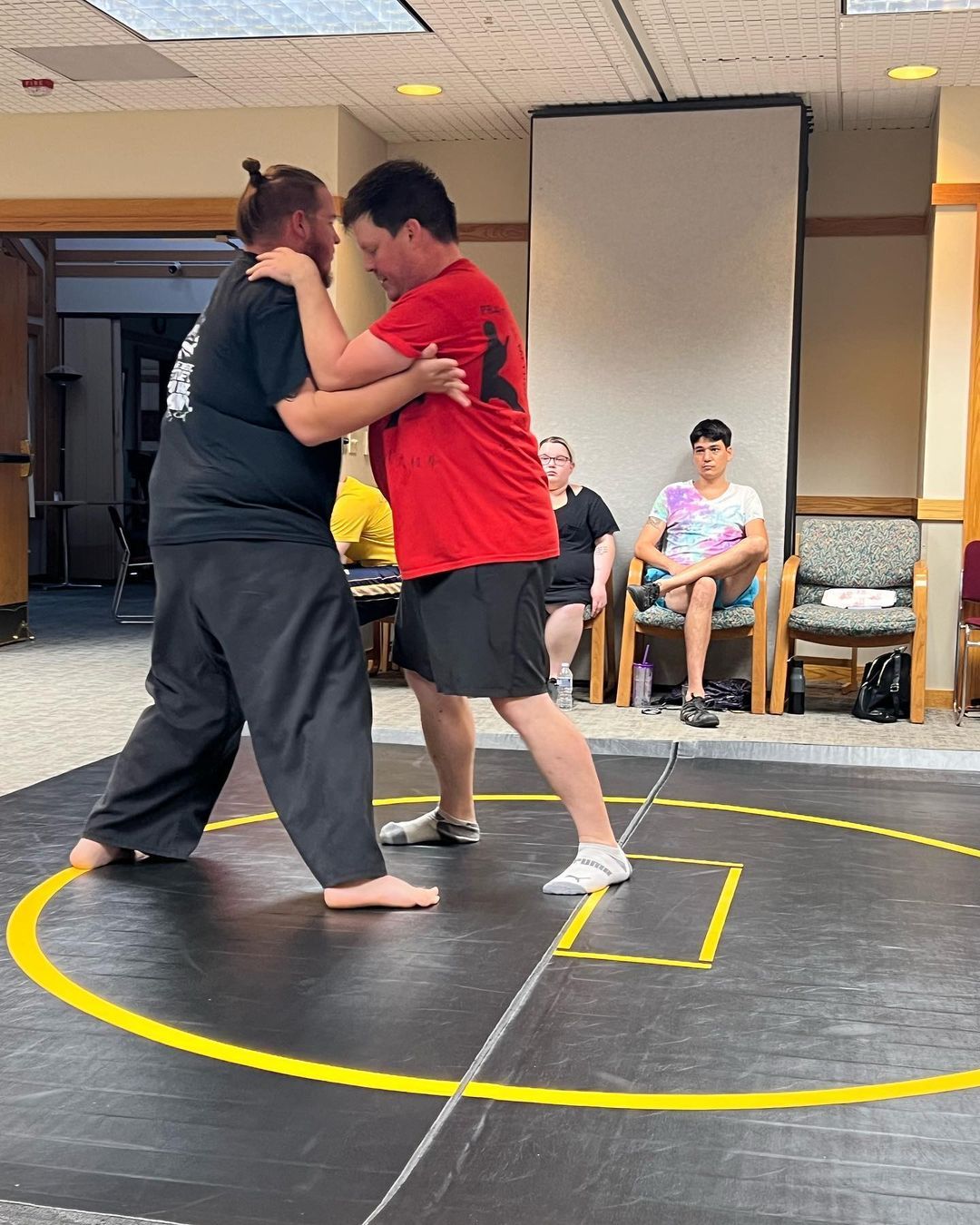 Two men are wrestling on a wrestling mat in a room.