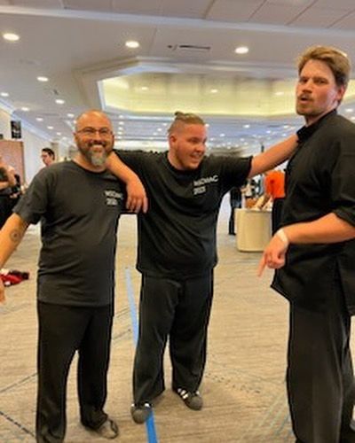 Three men in black shirts are standing next to each other in a room.