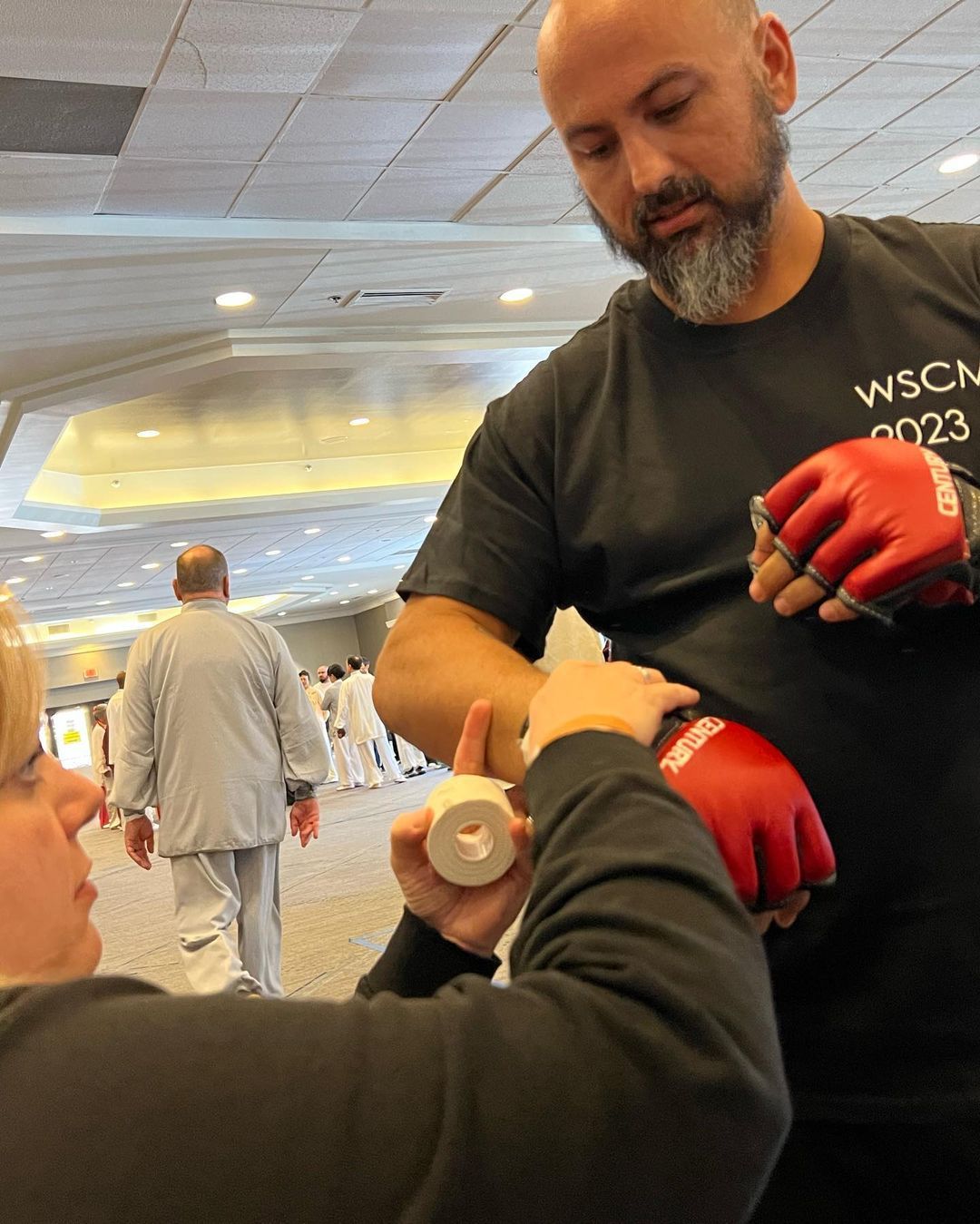 A man in a wscm shirt is helping a woman put on boxing gloves