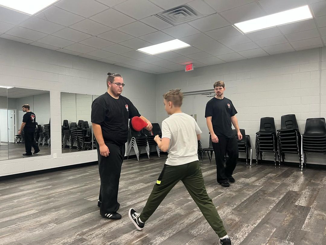 A man is teaching a boy how to box in a gym.