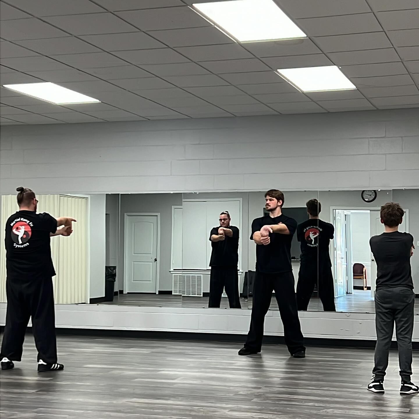 A group of people are practicing martial arts in front of a large mirror.